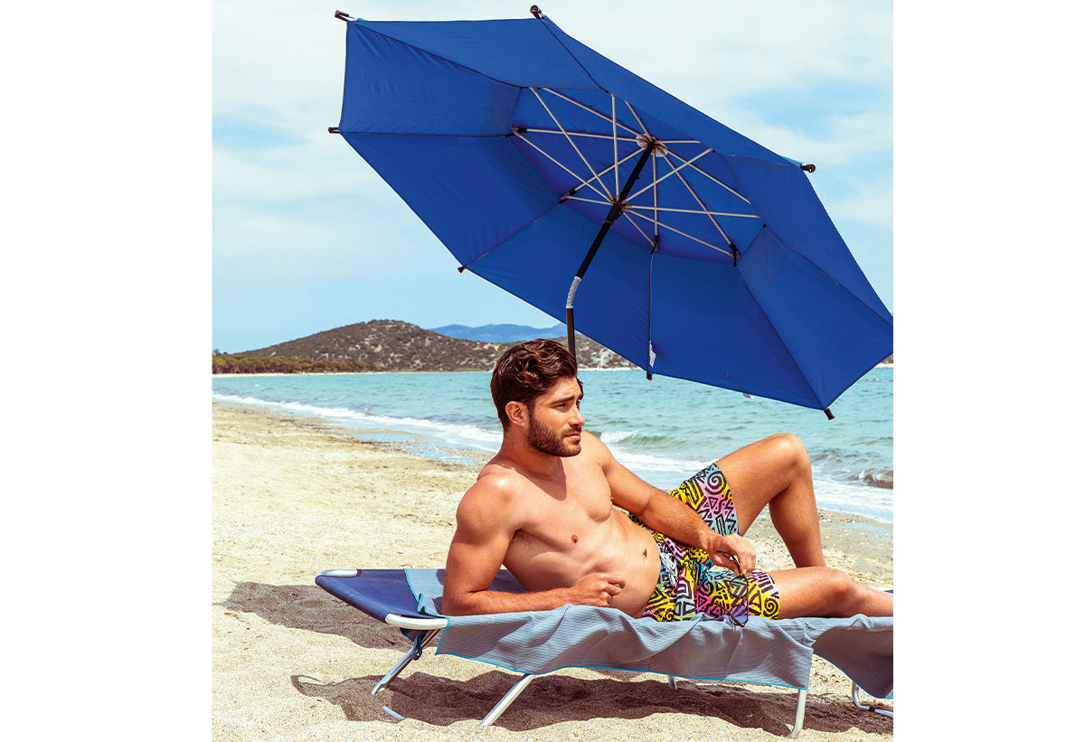 Ένας άντρας είναι ξαπλωμένος κάτω από την ομπρέλα σε μία ξαπλώστρα και το κοντάρι της ομπρέλας σε λειτουργία ανάκλησης.